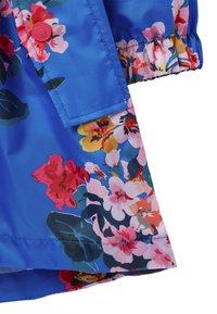 Blomstrede regnjakke med en livlig blå baggrund, der har pink, røde og gule blomster. Elastiske manchetter og en synlig mærkeknapdetalje.