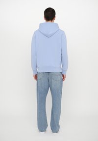 Vaaleansininen hupullinen collegepaita, jossa on pehmeä pinta, rento istuvuus ja resorikahleet, yhdistetty löysiin vaaleisiin farkkuihin.