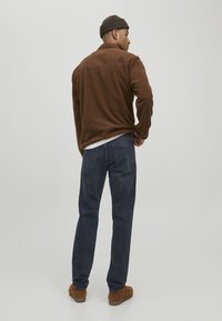 Chaqueta de forro polar marrón con cuello alto, combinada con jeans azul oscuro y zapatos de ante marrones. La tela tiene una textura suave.