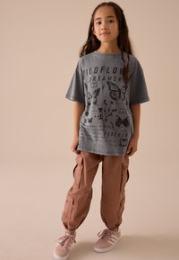 T-shirt gris oversize avec des motifs de papillons et de fleurs, associé à un pantalon cargo marron ample et des baskets roses.