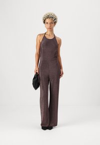 Jumpsuit halter de lentejuelas marrones con piernas anchas, que presenta un corpiño ajustado y una textura suave, complementado con un bolso de mano negro.