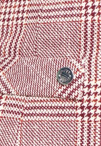 Tissu à motif pied-de-poule rouge et blanc avec un bouton en métal cousu sur une sangle ou un détail de manchette.