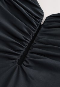 Gros plan d’un tissu noir avec un froncé élastique formant un détail de fente rassemblée et étirée.