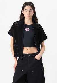 Black knit short-sleeve shirt jacket with a boxy fit, featuring blue trim and buttons, layered over a black crop top with pink embroidery.