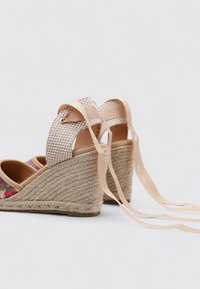 Sandalias de cuña con suela de yute, tejido geométrico en color beige y acentos en rosa, con largas tiras de cinta beige.
