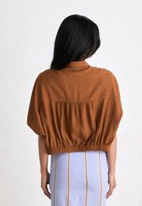Cropped top in rust fabric, featuring a loose fit, short sleeves, and an elastic waistband. Worn with a striped skirt.