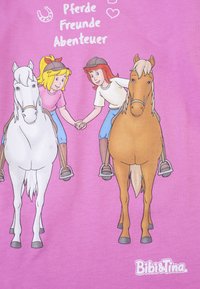 Maglietta rosa con due ragazze dei cartoni animati che si tengono per mano a cavallo, con un cavallo bianco e un cavallo marrone, e la scritta "Pferde Freunde Abenteuer."