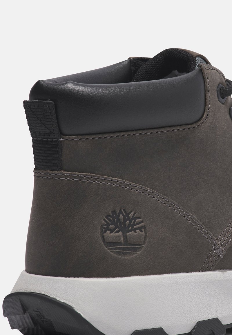 Botín de cuero gris oscuro con un cuello acolchado, detalles en negro, logo grabado y una suela de goma blanca con agarre texturizado.