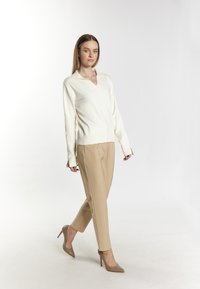 White v-neck sweater and beige tailored pants, combined with light brown high heels. The sweater has long sleeves and ribbed cuffs.