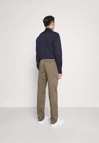 Camicia a maniche lunghe a fantasia navale con colletto standard abbinata a chinos beige e sneakers bianche. La camicia presenta un sottile motivo a pois.