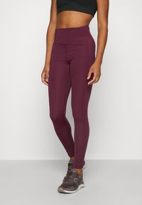 Burgundy, magas derekú leggings sima anyagból és oldalsó varratokkal. Szürke sportcipővel párosítva, amely fűzős és párnázott talppal rendelkezik.