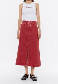 Rode denim maxirok met een vooraanzicht, hoge taille en ceintuurlussen. Gecombineerd met een nauwsluitend wit tanktop en zwarte flats met versiering.
