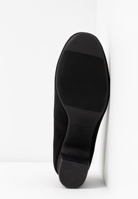 Bottine en suède noir avec une semelle lisse et une texture ribbed subtile. Présente un talon bas et un bout arrondi, taille 37 marquée sur la semelle.
