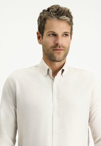 Camicia button-up beige chiaro con colletto strutturato, tessuto testurizzato e vestibilità slim con bottoni visibili lungo la parte anteriore.