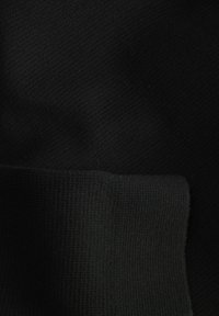 Zwart gebreide stof van dichtbij, met een gladde textuur en contrasterende geribde zoomdetail. Geen opvallende patronen of accenten zichtbaar.