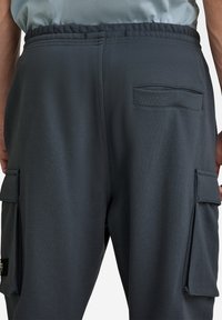 Joggers gris oscuro hechos de tela suave con cintura elástica y cordón, que cuentan con dos bolsillos laterales y un bolsillo trasero con solapa.