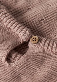 Roza pleten pulover z okrolim ovratnikom, ki ima teksturiran vzorec in lesen gumb kot poudarek na izrezu. Mehak tekstura preje.