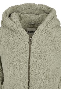 Chaqueta de felpa sherpa gris claro con capucha, cremallera metálica en la parte delantera y etiqueta "Urban Classics" en talla XS.
