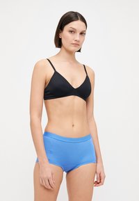 Crna bralette s podesivim naramenicama u kombinaciji s svijetloplavim boyshorts hlačicama s mekim pojasom. Tkanine djeluju glatko i oblikovano.