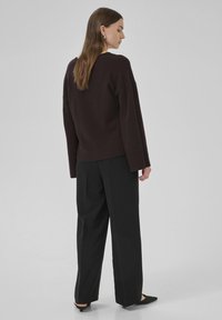Pull en maille marron foncé à coupe décontractée, avec des poignets et un ourlet côtelés. Associé à un pantalon noir ajusté et des chaussures noires à bout pointu.