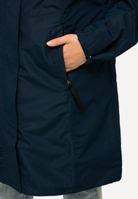 Giacca impermeabile blu navy con tasca laterale con zip, polsini elasticizzati e orlo dritto, caratterizzata da una texture liscia e un design minimalista.