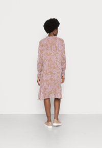 Vestido de mangas longas, transparente, em castanho claro com padrões florais em rosa. Apresenta uma saia com babados e mangas franzidas. Combinado com ténis claros.