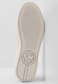 Sole di sneaker bianca con superficie testurizzata e antiscivolo. Presenta un logo MK circolare al centro. I bordi lisci si assottigliano verso il lato.