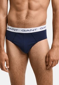 Marineblaue Baumwollunterhose mit einem weißen Bund, der das "GANT"-Logo trägt. Glatte Textur, taillierter Schnitt mit konturiertem Vorderteil und Seitennähten.
