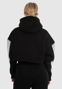 Zwarte cropped hoodie met grijze mouwen. Zacht katoen materiaal, met een grote capuchon en een brede, relaxte pasvorm. Naaddetails op de capuchon en mouwen.