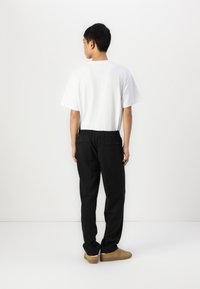 Pantaloni neri con elastico in vita, abbinati a una semplice t-shirt bianca. I pantaloni presentano una vestibilità comoda e discrete tasche posteriori. Sneakers marroni completano l'outfit.