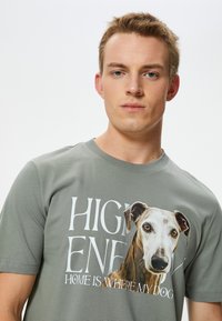 Camiseta de algodón gris con un gráfico de un perro grande y texto. Cuello redondo, mangas cortas, textura suave, con letras impresas en blanco.