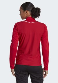 Red long-sleeve athletic top with a high collar, textured pattern, and white accents along the shoulders and collar. Black pants visible.