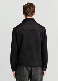 Veste en daim noire avec un col classique, un dos uni et des coutures discrètes. Associée à un pantalon en denim gris avec poches arrière.