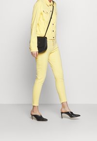 Giacca di jeans gialla e pantaloni con un design aderente. Mules in pelle nera con punta appuntita. Piccola borsa a tracolla nera, hardware minimale.