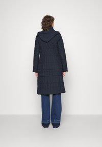 Abrigo acolchado azul marino con capucha, con un patrón diagonal y mangas largas, usado sobre jeans de pierna ancha con dobladillos desflecados.