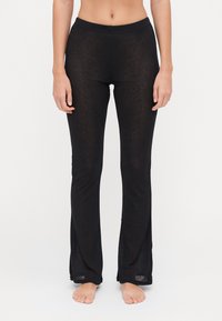 Schwarze, enganliegende Hosen aus einem leichten, halbtransparenten Stoff. Mit flachem Bund und seitlichen Schlitzen am Saum.