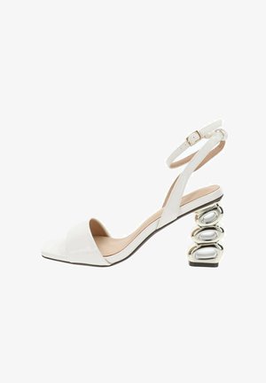 Sandalia blanca de punta abierta con correa en el tobillo y exclusivo tacón de bloque apilado metálico plateado esculpido.