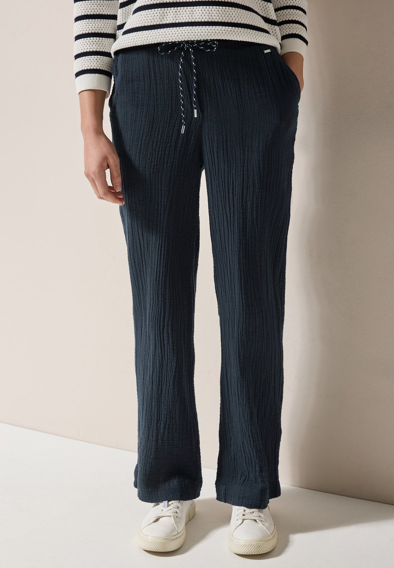 Pantaloni blu navy con trama, vita regolabile con cordoncino, design a gamba dritta e tasche laterali, abbinati a sneakers bianche.