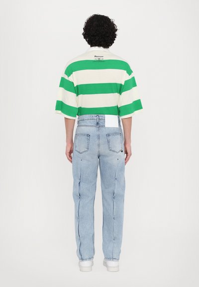 Groen en wit gestreept T-shirt met korte mouwen en een logo op de rug, gecombineerd met lichtblauwe, hooggepassende, losse jeans en witte schoenen.