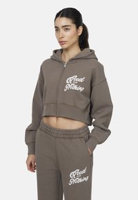 Felpa corta con zip in tessuto marrone, con stampa bianca "Good for Nothing". Abbinata a pantaloni coordinati con lo stesso logo.