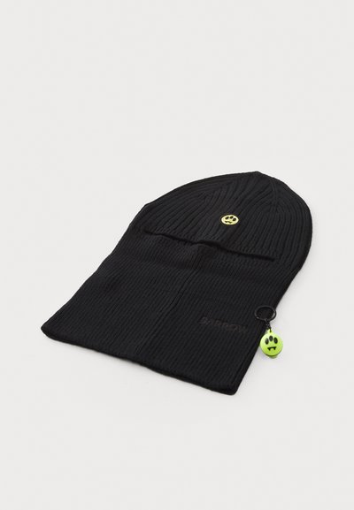 Berretto a maglia nero con texture a costine, caratterizzato da una piccola toppa gialla a forma di sorriso e un charm verde a forma di sorriso attaccato da un anello metallico.