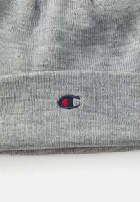 Grå stickad mössa i mjukt tyg, med en uppvikt design och ett broderat logo med röda och blå accenter framtill.