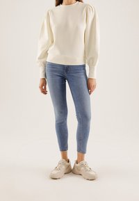 Krémový pulovr s balónovými rukávy, kombinovaný se světle modrými skinny džíny a béžovými teniskami. Hladká textura, jednoduch�ý design.