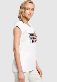 White cotton t-shirt with short sleeves, featuring a multicolored print of eyes in rectangular frames on the front. Smooth texture.