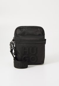 Borsa rettangolare nera realizzata in tessuto testurizzato, con un evidente logo "HUGO", chiusura con zip e tracolla regolabile.