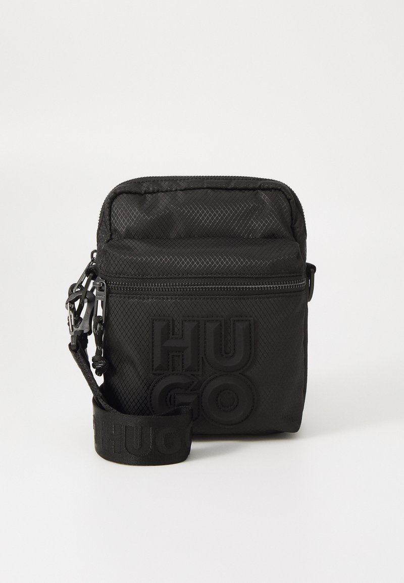 Borsa rettangolare nera realizzata in tessuto testurizzato, con un evidente logo "HUGO", chiusura con zip e tracolla regolabile.