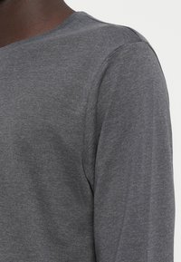 Grijze lange mouwen shirt gemaakt van zachte, gestructureerde stof. Heeft een ronde halslijn en subtiele naaddetails, met een ontspannen pasvorm rond de schouders.