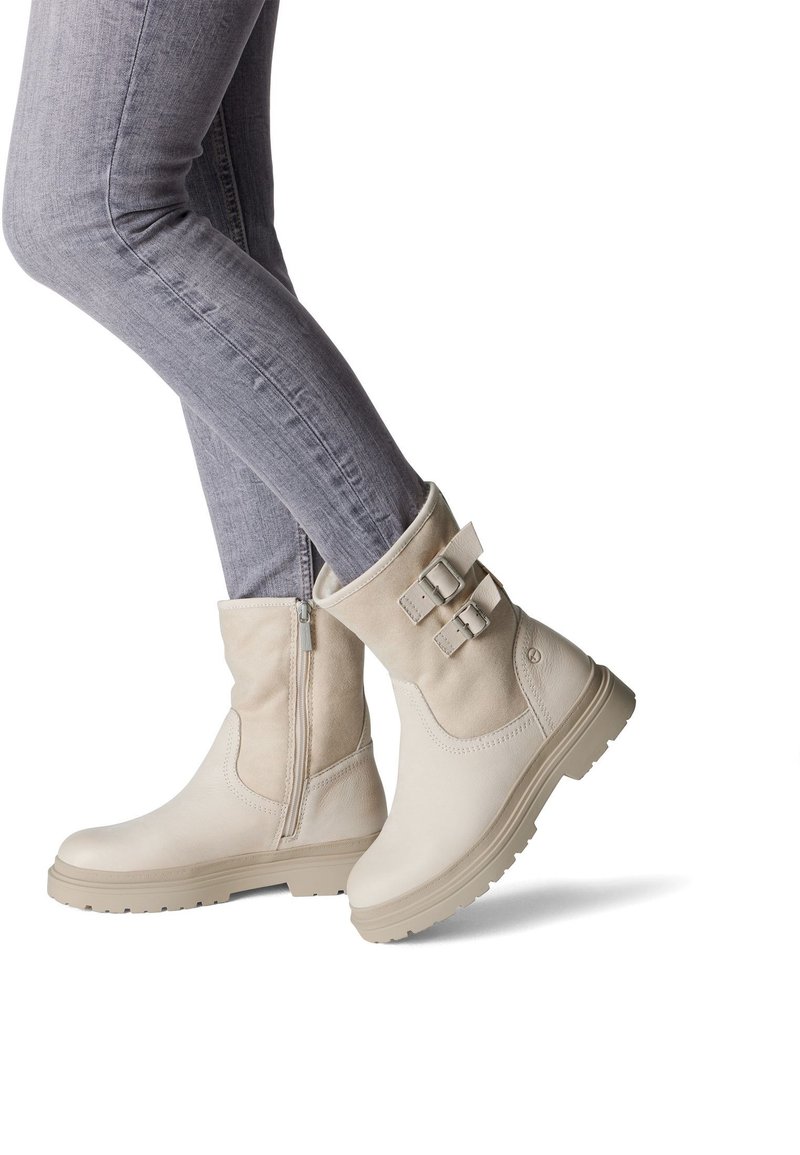 Bottes chevilles beiges avec une finition en cuir lisse, deux accents de boucle, une fermeture éclair sur le côté et une semelle en caoutchouc texturée.