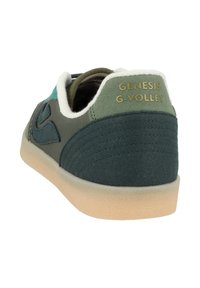 Dark green canvas sneaker with a textured rubber sole, featuring contrasting turquoise and beige accents, and "GENESIS G-VOLLEY" branding.