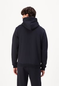 Marineblaue Kapuzenjacke aus weichem Material, mit einer großen Kapuze, langen Ärmeln und einem gerippten Saum, die eine glatte Textur aufweist.